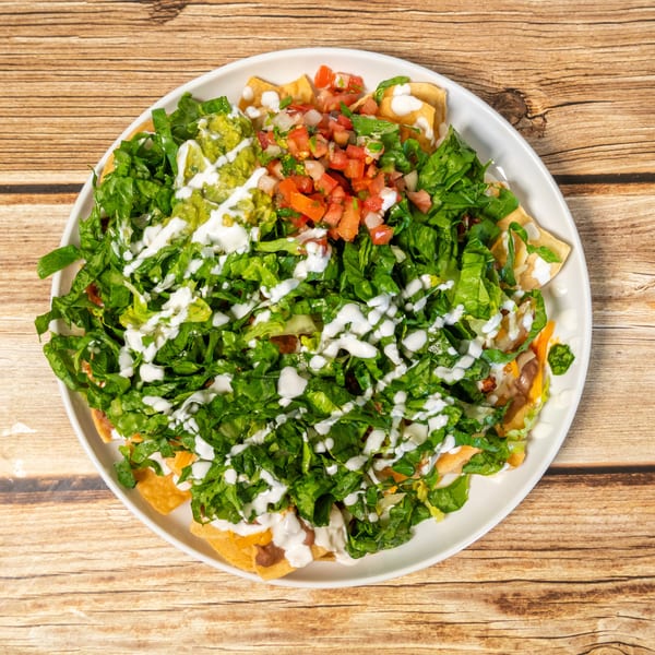 A large plate of nachos topped with lettuce, guacamole, pico de gallo, and sour cream.
