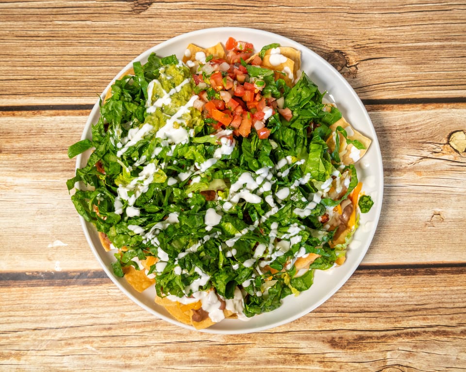 A large plate of nachos topped with lettuce, guacamole, pico de gallo, and sour cream.