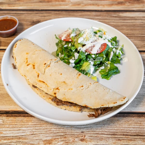 A large quesadilla with meat, a side salad with dressing, and two small sauce cups on a wooden table.