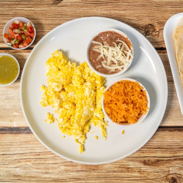 Scrambled eggs, refried beans with cheese, rice, salsa, pico de gallo, and tortillas on a wooden table.