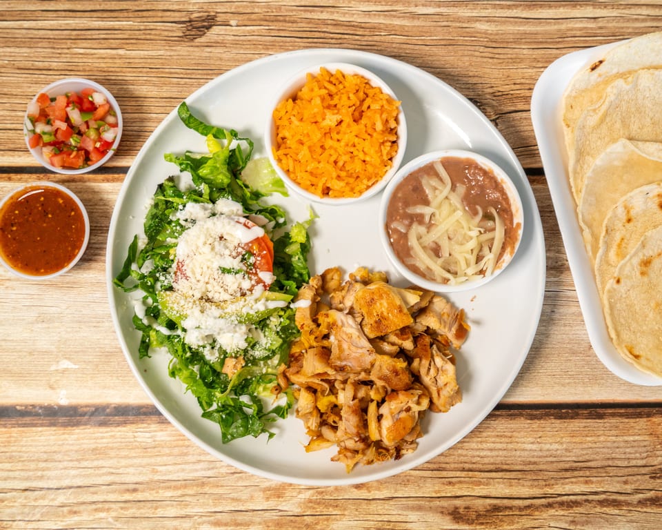 A Mexican dish with grilled chicken, rice, beans, salad, salsa, pico de gallo, and tortillas.