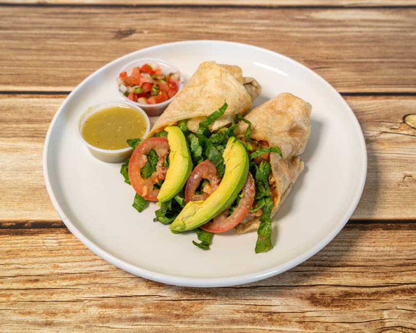 Two burritos with lettuce, tomato, and avocado slices, served with salsa and green sauce.