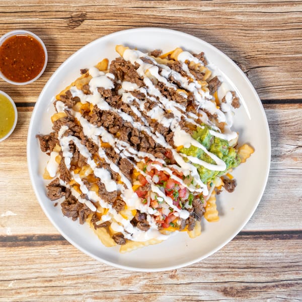Loaded fries with carne asada, guacamole, pico de gallo, and sour cream, with two salsa cups.