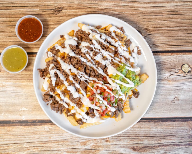 Loaded fries with carne asada, guacamole, pico de gallo, and sour cream, with two salsa cups.