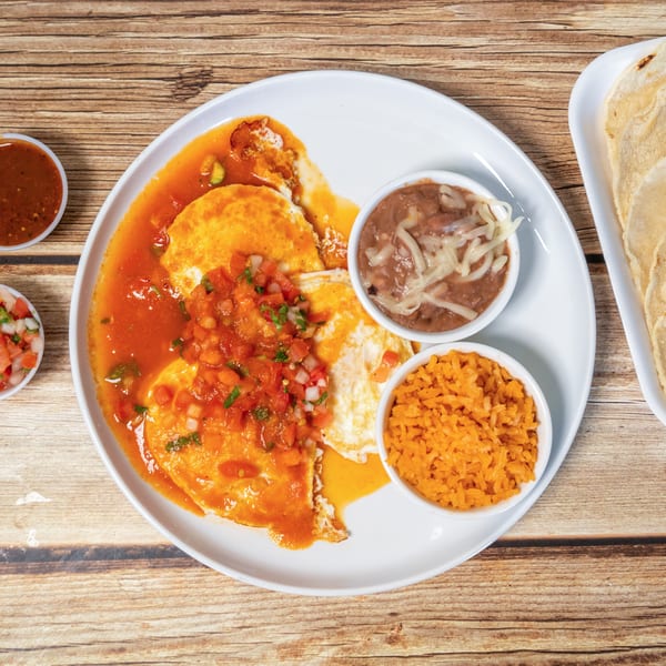 Huevos rancheros with rice, beans, salsa, and tortillas on a wooden table.
