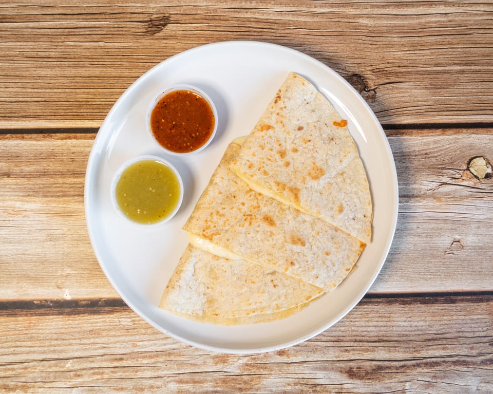 Cheese quesadillas with red and green salsa on a white plate, on a wooden table.