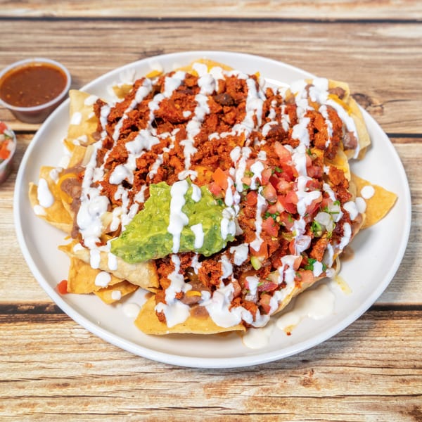 A plate of nachos with chorizo, guacamole, pico de gallo, and crema, with salsa on the side.