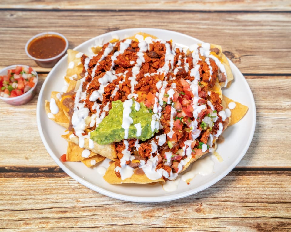 A plate of nachos with chorizo, guacamole, pico de gallo, and crema, with salsa on the side.