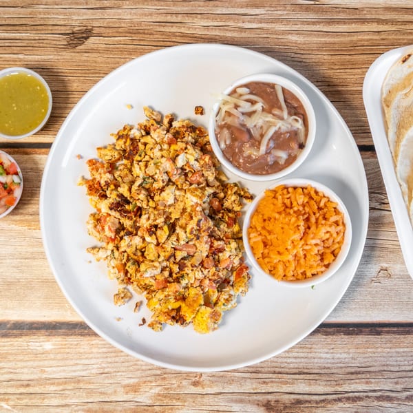 Scrambled eggs with pico de gallo, rice, beans, salsa, and tortillas on a wooden table.