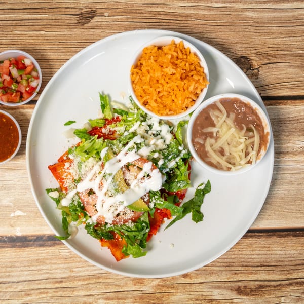 Mexican dish with enchiladas, rice, beans, salsa, and pico de gallo on a wooden table.